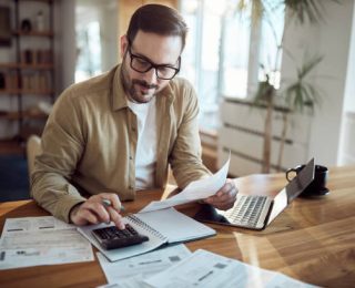 Young man using calculator while working on his financial plans at home.