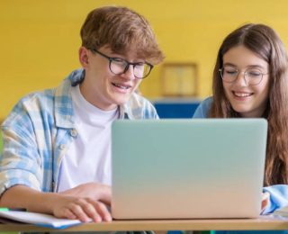 High school students sitting at the desk in the classroom during lesson and talking. Teenage girl and boy using laptop together.